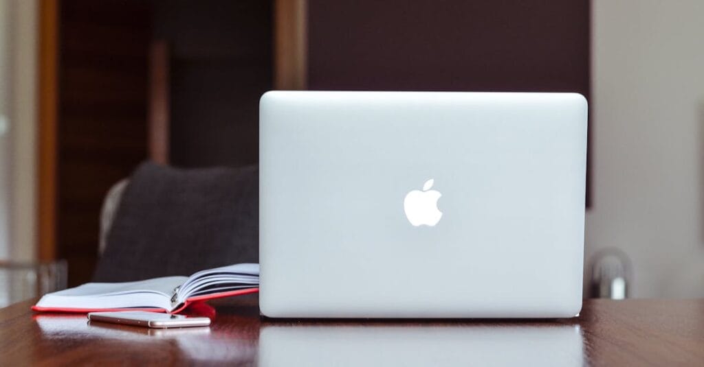 A clean and modern workspace featuring a laptop, book, and smartphone on a wooden table.