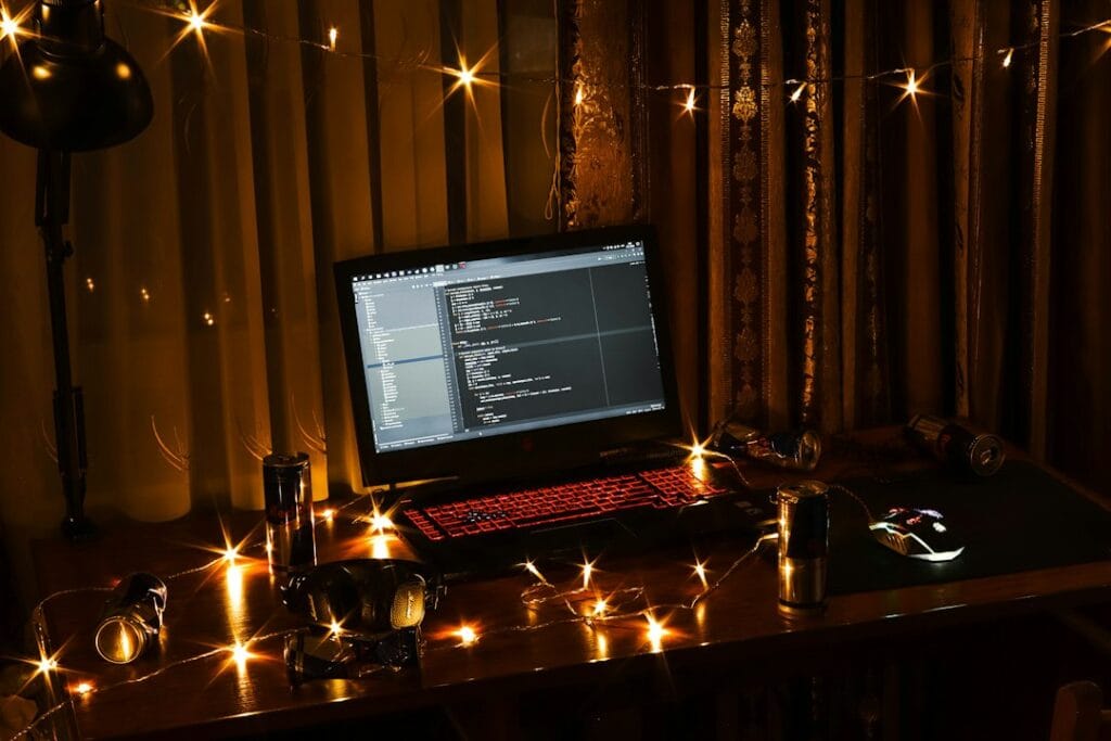 Laptop with a backlit keyboard on a desk surrounded by string lights