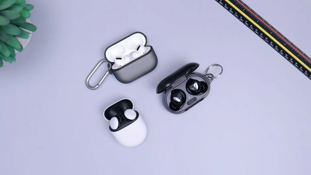 Three pairs of wireless earbuds in open charging cases on a desk