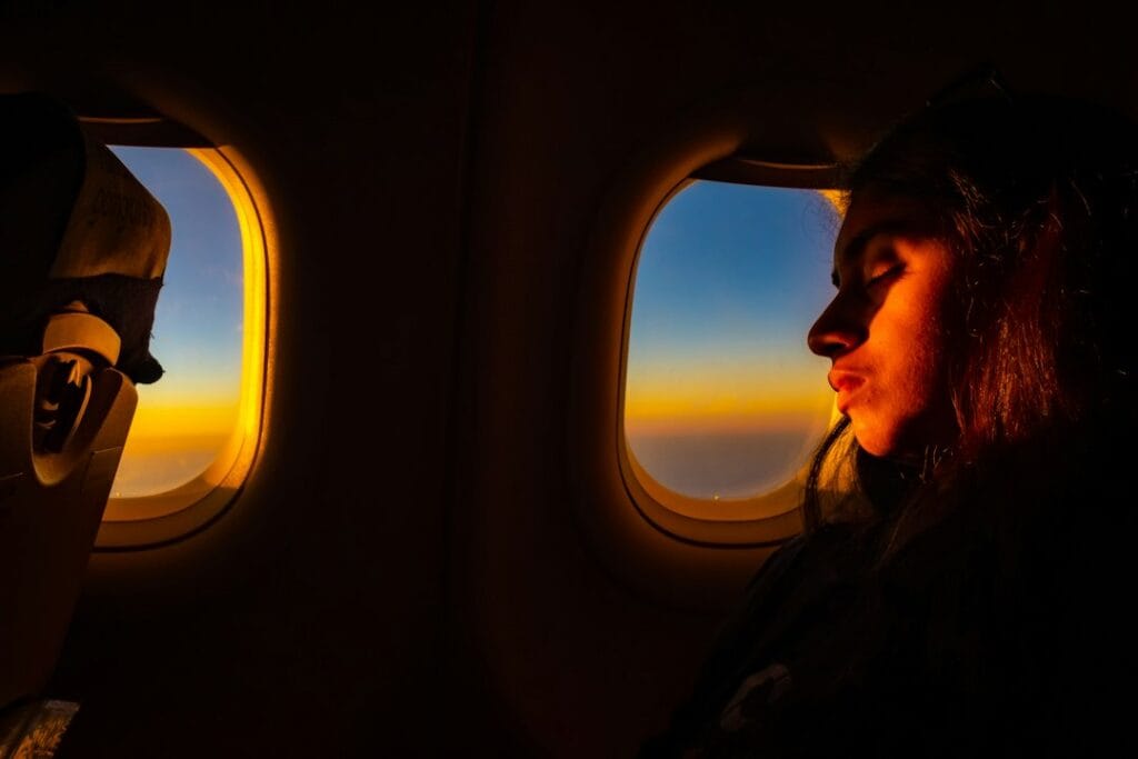 A woman looking out an airplane window at sunset