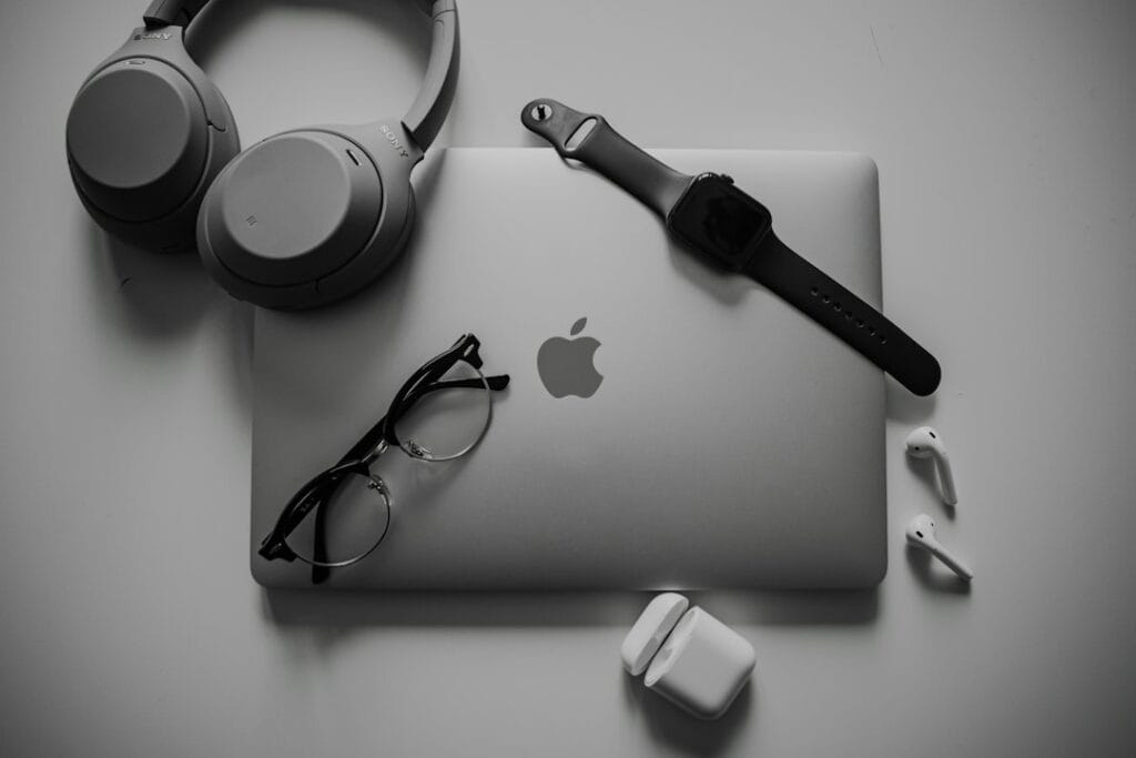 Headphones, glasses and wireless earbuds on a desk next to a laptop