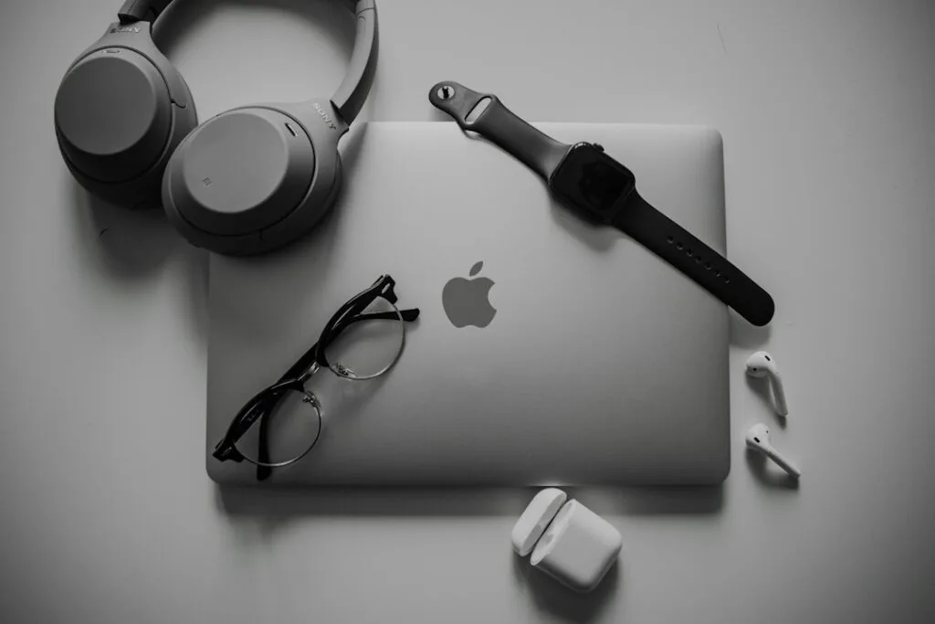 Headphones, glasses and wireless earbuds on a desk next to a laptop